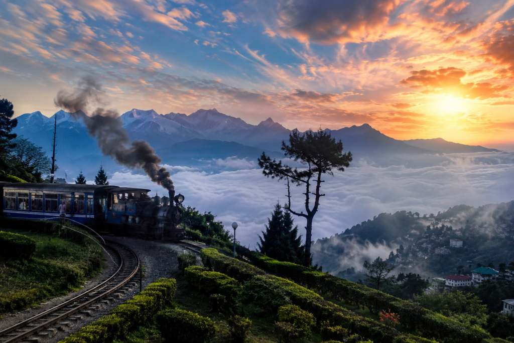 Darjeeling Toy Train at sunrise with lush tea plantations, Himalayan mountain views, mist-covered valleys, and scenic railway tracks in West Bengal.